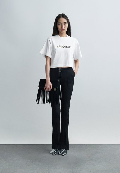 Λευκό κοντό t-shirt με το λογότυπο "Off-White", μαύρο ψηλόμεσο παντελόνι με καμπάνα, τσάντα φάκελος με κρόσσια και μεταλλικά παπούτσια με τακούνι.