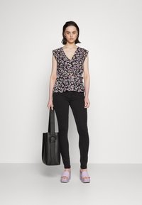 Top com estampa floral em preto, rosa e verde; mangas curtas com babados; decote em V. Combinado com jeans skinny pretos e saltos plataforma lavanda.