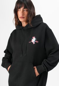 Black hoodie made of soft fabric, featuring a front pocket and drawstring hood. Centered graphic with pink and blue accents.