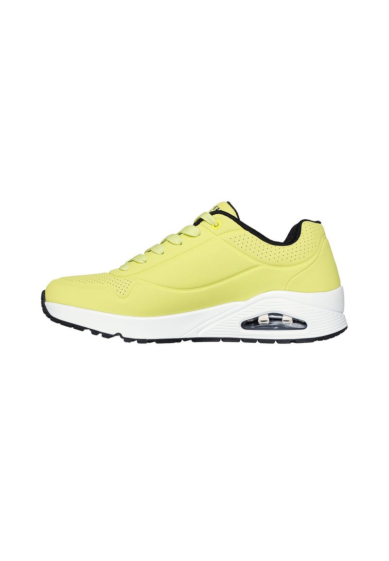 Helle gelbe Sneaker mit einer glatten Oberseite, schwarzen Akzenten, Schnürdesign und sichtbarer Luftpolsterung in der weißen Zwischensohle. Strukturiertes Profil.
