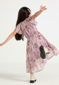 Blommig klänning i ljuslila med elastisk midja, korta ärmar och kjol i lager. Har blommönster i rosa och grönt. Svartsulade stövlar.