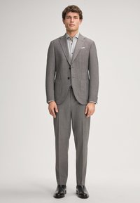 Completo a quadri grigio con giacca a due bottoni e rever a punta, abbinato a una camicia grigia chiara e scarpe nere.