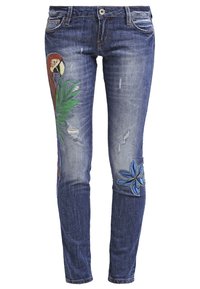 Vaqueros de mezclilla azul con corte slim, que presentan un loro y una planta tropical bordados en la pierna izquierda y una flor azul en la rodilla derecha.