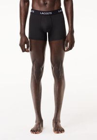 Fekete pamut bokszernadrág, testhez simuló fazonnal, kontrasztos fehér "LACOSTE" logóval a gumis derékszíjon.
