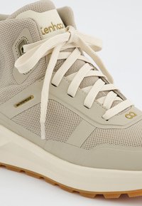 Beżowe wodoodporne sneakersy z siateczkową cholewką, wyściełanym kołnierzem, płaskimi sznurówkami oraz teksturowaną gumową podeszwą z gumowym spodem. Obecne są złote akcenty.