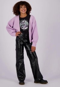 Violets trikotāžas kardigans, melna grafiska T-krekls un melnas platām kājām mākslīgās ādas bikses. Modelis valkā melnus zābakus.