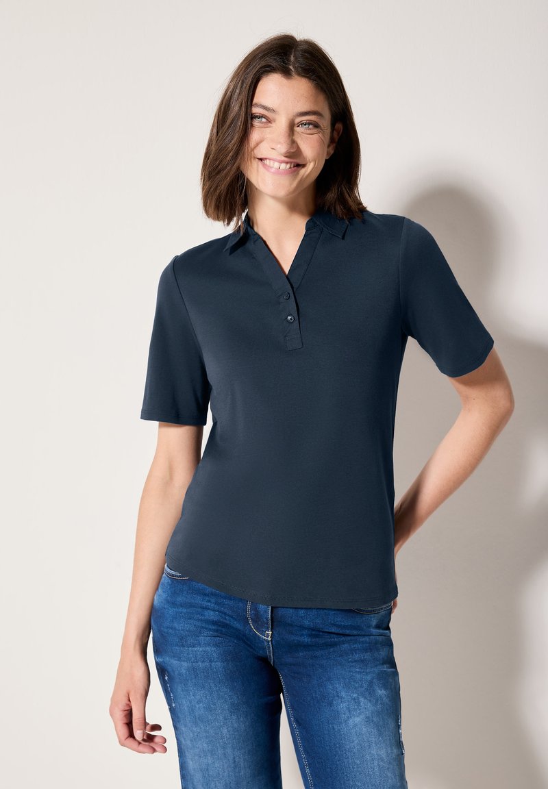 Námořnický polo top s krátkým rukávem, knoflíkovým límcem a hladkou texturou. Nosit s modrými džíny, které mají volný střih a čisté linie.