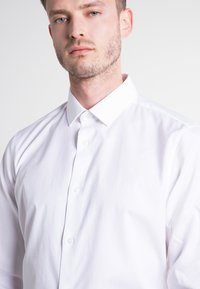 Weißes Langarmhemd mit klassischem Kragen, aus glattem Baumwollstoff gefertigt. Verfügt über eine Knopfleiste und einen schlichten, taillierten Schnitt.