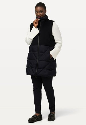 Gilet imbottito blu navy con colletto alto e parte superiore nera in contrasto. Presenta una texture trapuntata, chiusura con zip e tasche laterali.