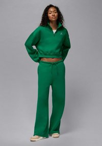 Zielona krótka bluza z wysokim kołnierzem i haftowanym logo, zestawiona z pasującymi luźnymi spodniami dresowymi na regulowanym pasku.