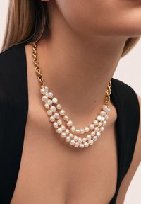 Collar de perlas de tres hilos con perlas blancas irregulares intercaladas con cuentas de oro, unidas a una cadena de eslabones de oro.