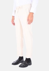 Pantaloni color crema con una vestibilità rilassata, vita elasticizzata e orli cuffi, abbinati a scarpe in pelle nere e calze scure.