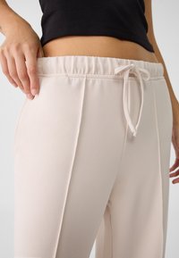 Svetle růžové, vysoko pasové jogger kalhoty s elastickým pasem a šňůrkou. Hladká textura, obsahuje vertikální švy.