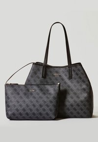 Dwie czarne torby Guess z monogramem: jedna duża torba na ramię z paskami na ramię oraz mniejsza torba na zamek błyskawiczny z paskiem na nadgarstek.