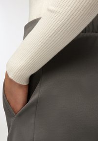 Szara sukienka z gładkiego materiału i bocznymi kieszeniami, zestawiona z białą, prążkowaną bluzką z długim rękawem, z widocznymi detalami rękawów w pobliżu kieszeni.