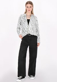 Jachetă cu model zebră în nuanțe de gri și alb, cu fermoar, asortată cu pantaloni negri, cu talie înaltă, și adidași negri. Dispune de mâneci lungi și un croi lejer.