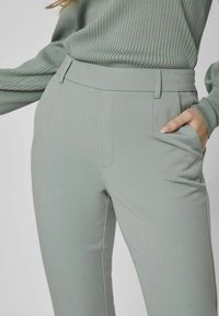 Vaaleanvihreät muotoillut housut, jotka on valmistettu sileästä kankaasta. Housuissa on tasainen etuosa, sivutaskut ja slim fit -muotoilu.