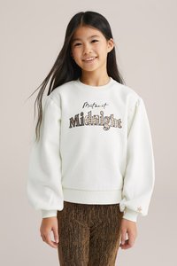 Fehér pulóver puffos ujjal, fekete és arany "Midnight" felirattal, barna struktúrájú leggingssel, arany akcentussal párosítva.