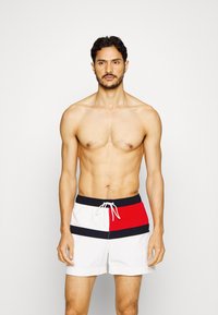 Costume da bagno bianchi, con righe orizzontali rosse e blu navy. Materiale leggero con vita elastica e dettaglio con cordino.