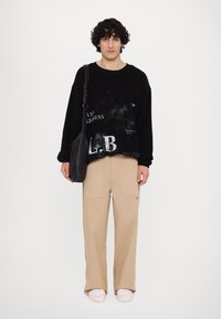 Sweatshirt noir surdimensionné avec des impressions graphiques blanches, assorti à un pantalon beige à jambes larges et des baskets blanches. Accessoirisé avec un sac noir.