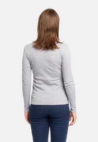 Camicia grigia a maniche lunghe con un design aderente, realizzata in materiale morbido, abbinata a jeans blu scuri. Vista di spalle, con capelli alla spalla.