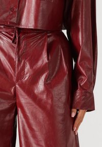 Bordeauxkleurige outfit van imitatieleren met een cropped jasje en een broek met hoge taille, voorzien van een gestructureerde afwerking en voorzakken.