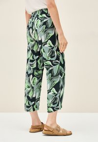 Kalhoty s květinovým potiskem a elastickým pasem, s velkými zelenými a černými listy na tmavém pozadí; zkrácený a volný střih.