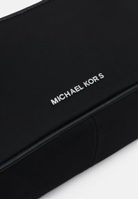 Czarna nylonowa kosmetyczka o gładkiej fakturze, z srebrnym logo "MICHAEL KORS" na przodzie, w prostokątnym kształcie i subtelnymi szwami.