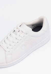 Sneaker bianca in pelle con dettagli perforati sui lati, lacci bianchi e marchio Fila sul lato. Texture liscia con un design semplice.