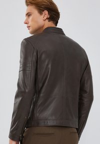 Giacca di pelle marrone con una texture liscia, design aderente e dettagli a coste sulle spalle. Caratterizzata da una zip frontale e tasche laterali.