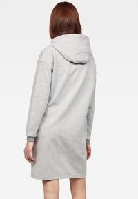 Grå sweatshirtklänning med stor huva, lång ärm och knälång skärning. Mjuk textur med ribbade mudd och nederkant. Enkelt mönster.