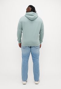 Muntgroen hoodie met een relaxed fit en geribbelde manchetten, gecombineerd met lichtblauwe straight-leg jeans en beige sneakers.