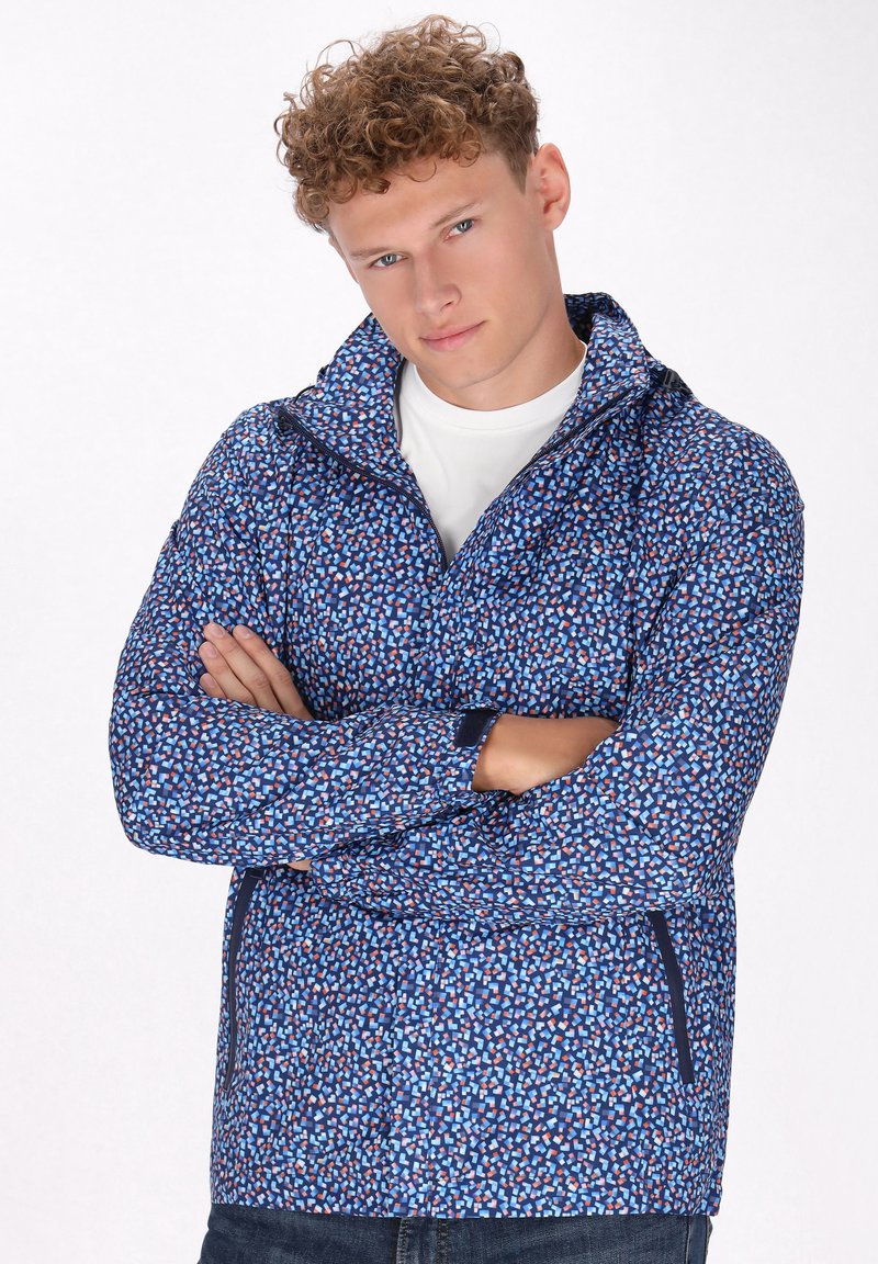 Giacca blu leggera con un motivo geometrico in rosso e bianco. Presenta una chiusura con zip, colletto alto e dettagli a contrasto in navy.
