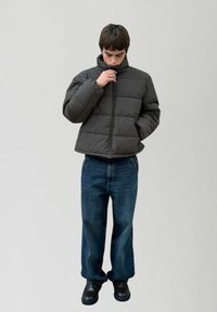 Ciemnoszara kurtka puchowa z wysokim kołnierzem, poziomym pikowaniem; dopasowana do szerokich niebieskich dżinsów i czarnych butów.