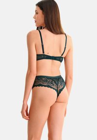 Ensemble de lingerie en dentelle vert foncé comprenant un bralette avec des bretelles réglables et un string assorti avec des bords festonnés et des motifs floraux.