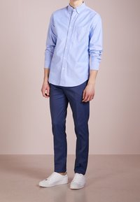 Jasnoniebieska koszula z długim rękawem i kieszonką na piersi, w połączeniu z granatowymi spodniami i białymi trampkami. Prosty, luźny krój.