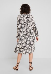 Sukienka z długim rękawem z lekkiego materiału, z czarno-kremowym wzorem kwiatowym, w długości do kolan i luźnym kroju. W zestawie z sandałami na paski.