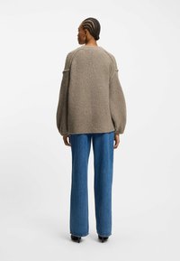 Overmaat, getextureerde, bruine trui met raglanmouwen. Gecombineerd met lichtblauwe flared jeans, die een ontspannen pasvorm en gladde stof tonen.