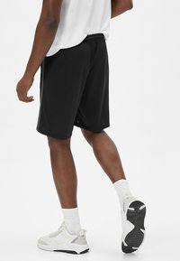 Sorte atletiske shorts lavet af letvægtsstof, med en elastisk talje og en afslappet pasform, parret med hvide sneakers og ankelstrømper.