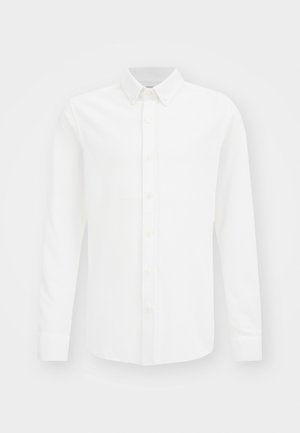 Chemise blanche à manches longues avec un col boutonné et un devant uni sur fond blanc.