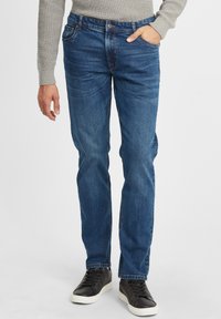 Slim-fit modre kavbojke z rahlim zbledelostjo, zasnova s petimi žepi in kontrastnim šivanjem. V kombinaciji z črnimi nizkimi športnimi čevlji.