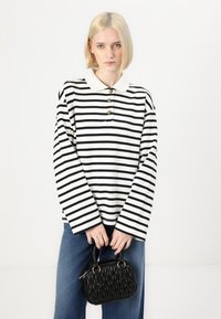 Black and white striped long-sleeve polo shirt with a collar and three gold buttons, paired with blue denim jeans and a textured black handbag.