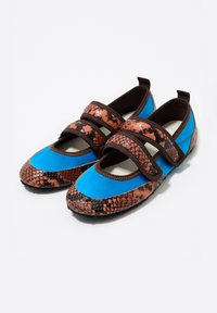 Par de zapatos planos con tela azul y correas y ribetes de estampado de serpiente marrón, que presentan cierres de velcro y suelas de goma negras.
