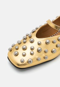 Scarpa Mary Jane in pelle dorata con embellishments in metallo argentato, punta quadrata e cinturino alla caviglia. Suola nera completa il design.