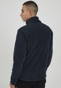 Sudadera de forro polar en color marino con un cuello alto, mangas largas y textura suave. Presenta un diseño simple y elegante sin hardware visible ni patrones.