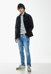 Blå denimjeans kombinerade med en ljusgrå tröja och en svart jacka; avslappnad skor med en beige och vit färgskala.