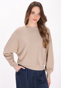 Beige, lichtgewicht, gestructureerde trui met een losse pasvorm, een bootnek en lange, afgewerkte mouwen, gecombineerd met marineblauwe satijnen broeken.