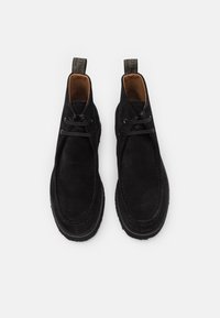 Gli stivaletti in suede neri presentano una punta rotonda, un interno contrastante marrone, un design con lacci e una suola in gomma testurizzata con linguette per il tallone.