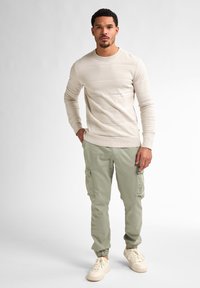 Beige long-sleeve textured shirt with horizontal stripes, paired with light green cargo pants featuring side pockets and elastic cuffs. Cream sneakers.