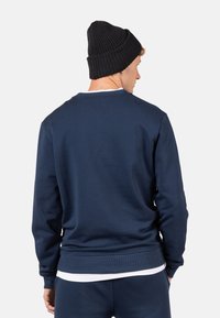Felpa navy a collo rotondo con polsini e orlo a coste, caratterizzata da una texture liscia. Abbinata a un berretto di maglia nero. Design semplice, senza motivi.